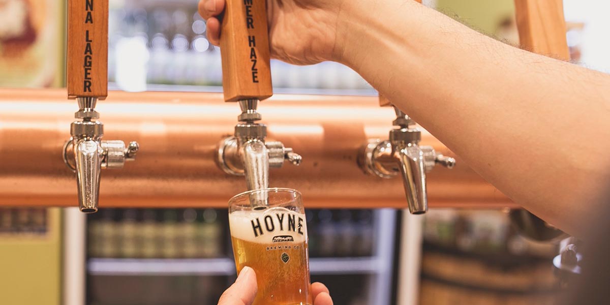 A person pouring beer into a Hoyne beer glass from a tap.