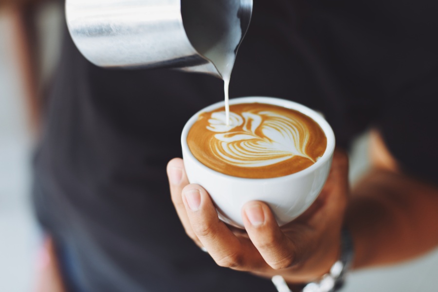 A person pouring milk into a latte.