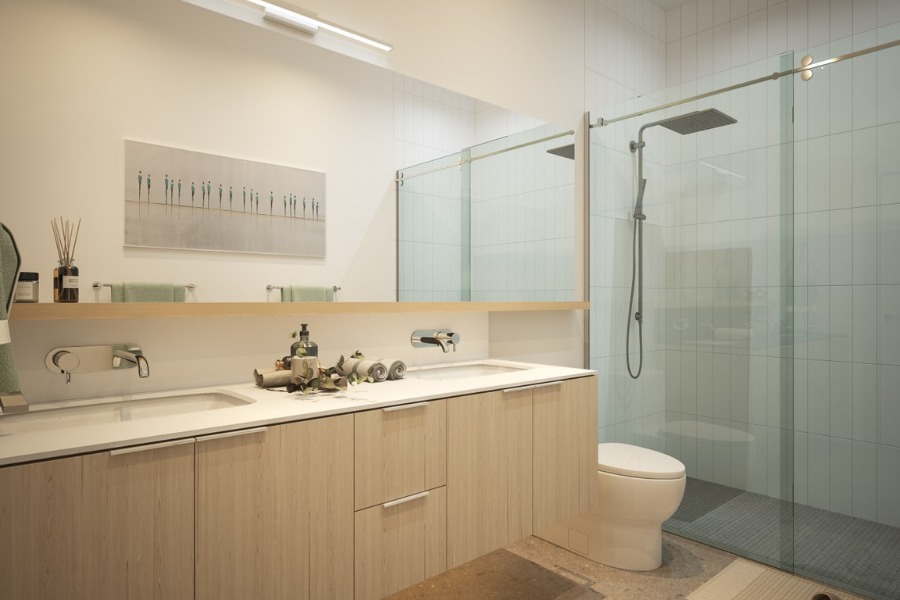 The Rise on Fifth's rendering of a bathroom with two sinks, light wood finishes, a white countertop and toilet and a walk-in glass shower.