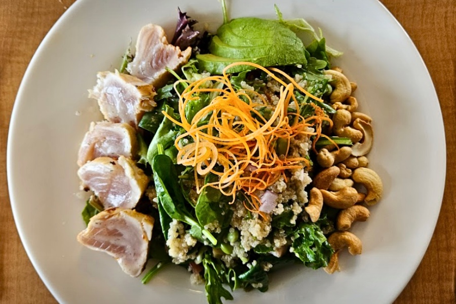 A bowl of delicious food including tuna, nuts, avocado and fresh greens.